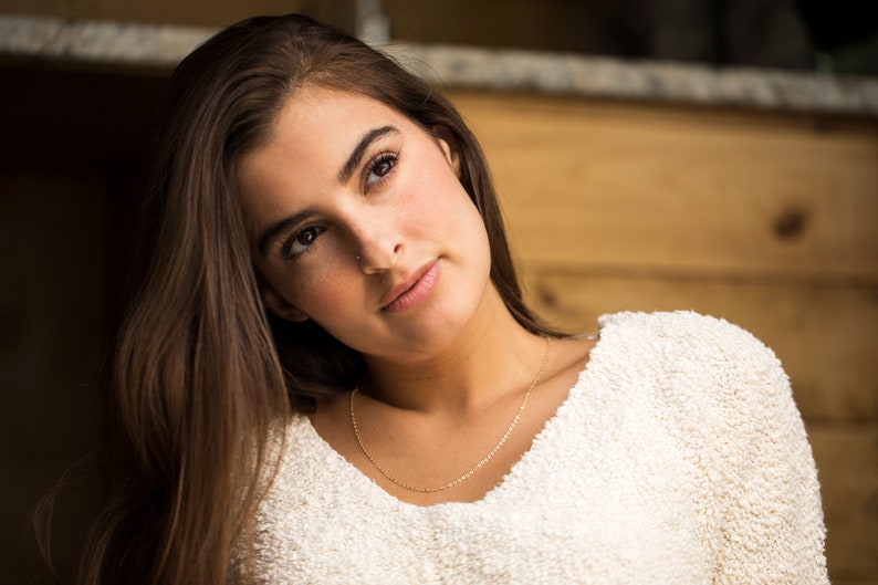 May include: A young woman with long brown hair wearing a white fuzzy sweater and a gold chain necklace. She is looking up and to the right.