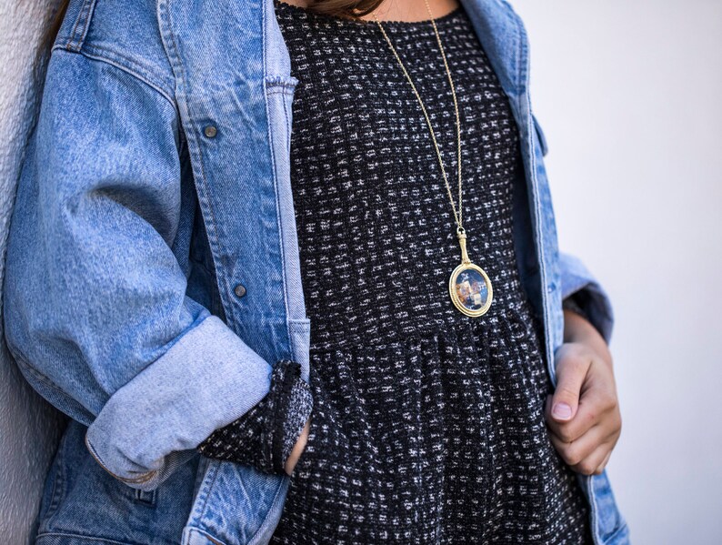 Puede incluir: Una mujer lleva una chaqueta vaquera azul sobre un vestido estampado en blanco y negro. Lleva un collar de cadena dorada con un colgante redondo.