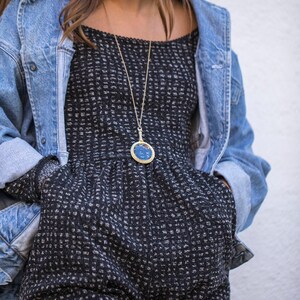 Puede incluir: Una mujer con un vestido de estampado blanco y negro con una chaqueta vaquera. Lleva un collar de oro con un colgante azul.