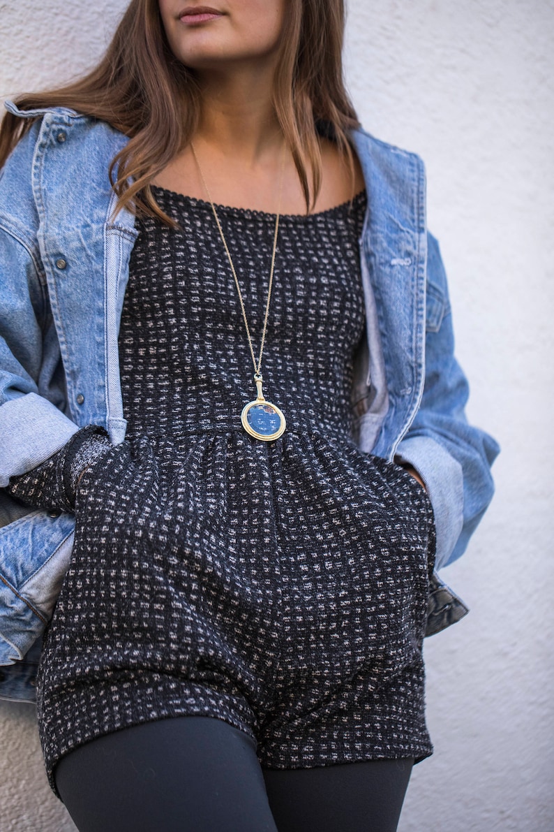Puede incluir: Una mujer con un vestido de estampado blanco y negro con una chaqueta vaquera. Lleva un collar de oro con un colgante azul.