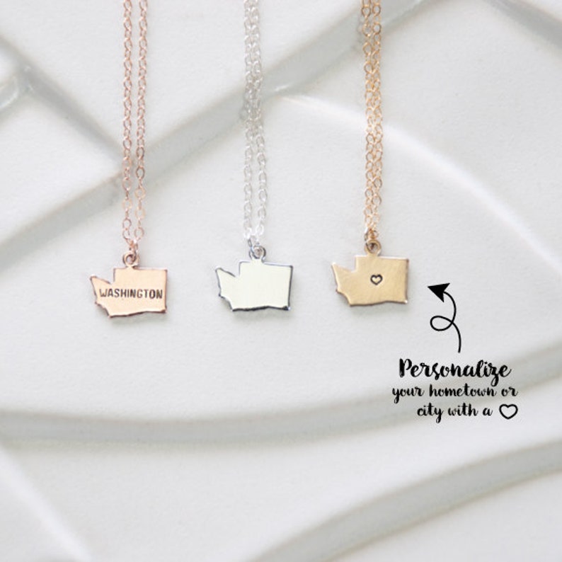 May include: Three gold necklaces with state of Washington pendants. The pendant on the left says "WASHINGTON". The middle pendant is plain. The pendant on the right has a small heart cutout. The text below the necklaces says "Personalize your hometown or city with a heart."