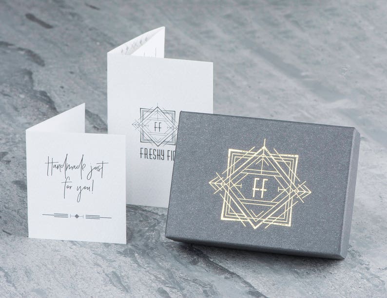 May include: A gray box with a gold geometric design and the letters "FF" in the center. The box is sitting on a gray surface. The text "Handmade just for you!" is on a white card.