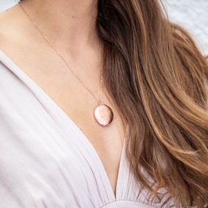 Op de afbeelding: Een ros&eacute;gouden ketting met een delicate ketting en een ronde hanger. De hanger heeft een getextureerd oppervlak en een licht gehammerde afwerking.