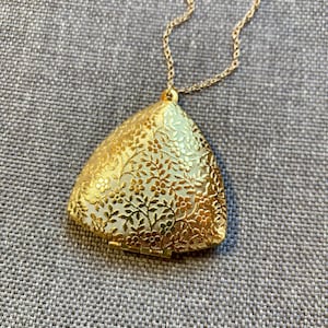 May include: A gold-tone necklace with a triangular pendant featuring a floral design. The pendant has a hinged opening.