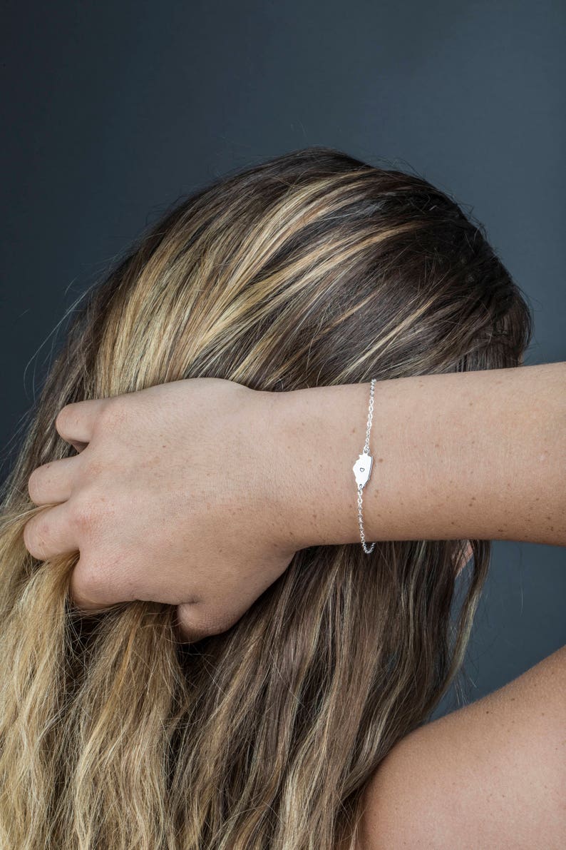 May include: A silver chain bracelet with a small, heart-shaped charm. The charm has a single, small diamond in the center.