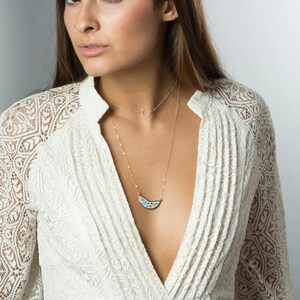 May include: A woman wearing a white lace dress with a gold necklace featuring a crescent moon pendant with a colorful mosaic design.