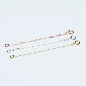 May include: Three delicate chain extenders in rose gold, silver, and gold. Each extender features a small, round clasp on one end and a matching ring on the other. These are ideal for adjusting the length of necklaces or bracelets.