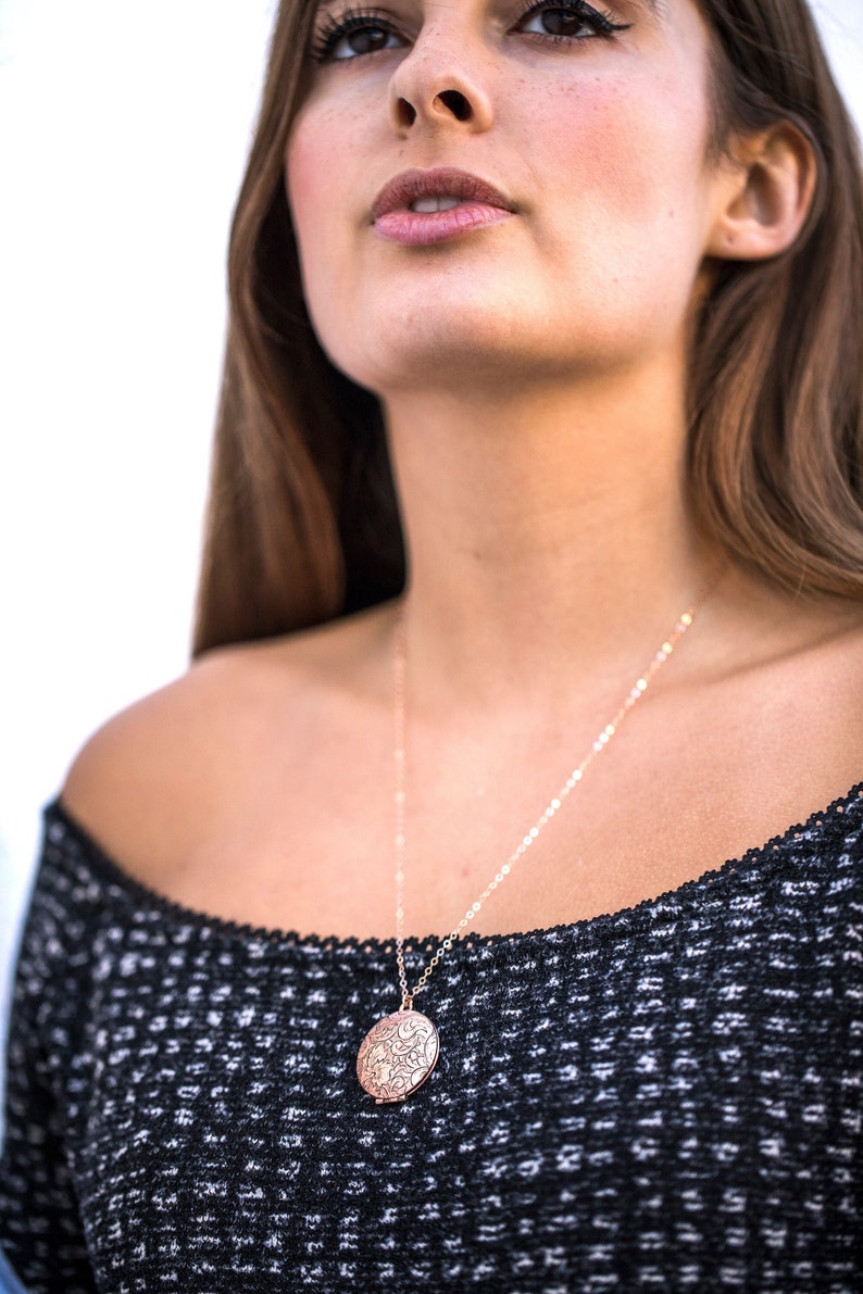 Op de afbeelding: Een vrouw draagt een zwarte off-shoulder trui met een delicate gouden kettingketting en een ronde, ros&eacute;gouden hanger.
