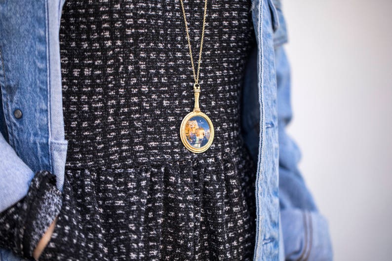 Puede incluir: Un vestido con estampado en blanco y negro con un collar de cadena dorada que presenta un colgante redondo con una imagen colorida en su interior.