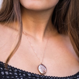 Op de afbeelding: Een close-up van een vrouw die een zwart topje draagt met een delicate gouden ketting met een rond, versierd medaillon.