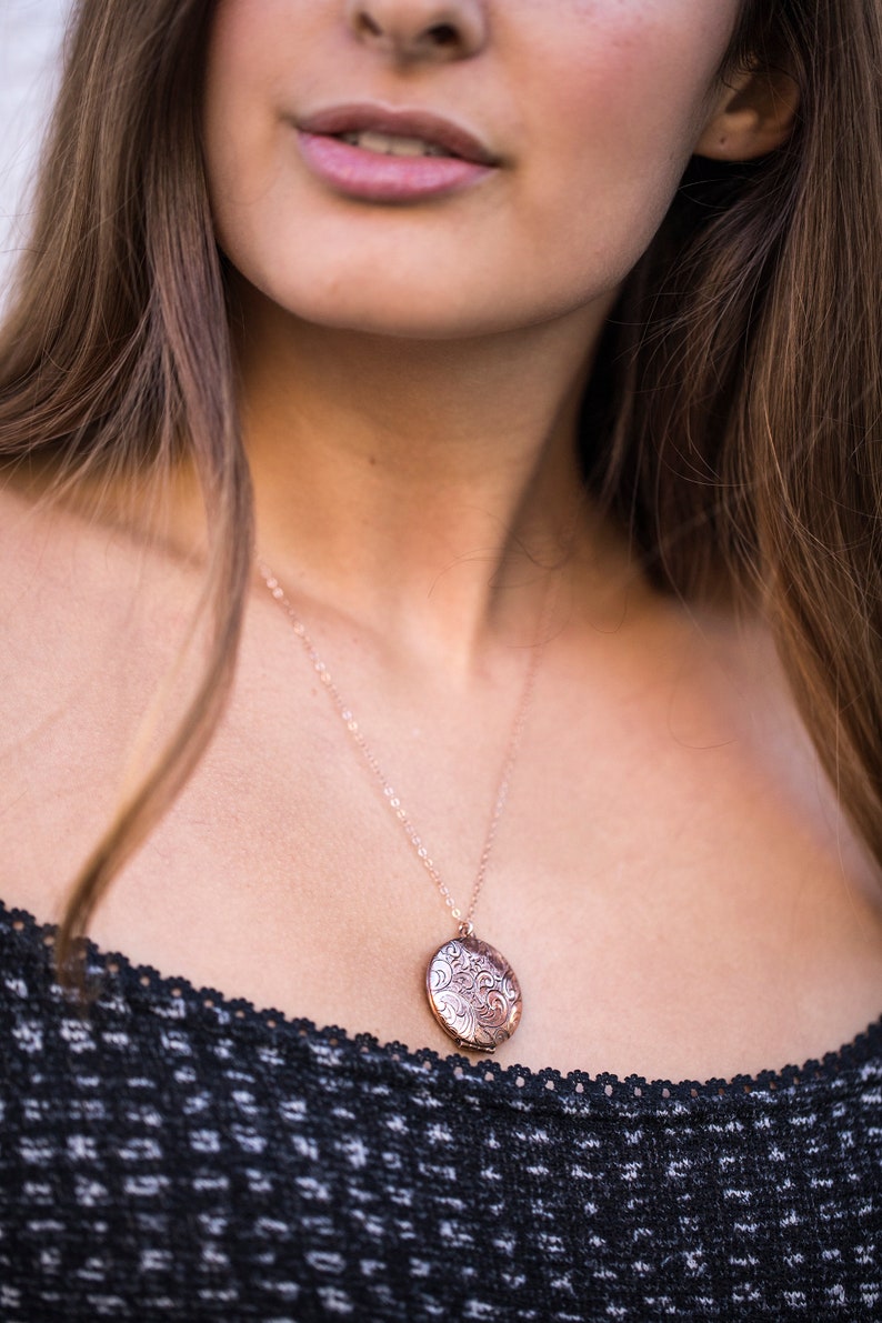 Op de afbeelding: Een close-up van een vrouw die een zwart topje draagt met een delicate gouden ketting met een rond, versierd medaillon.