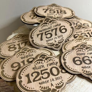 May include: A close-up of a pile of wooden signs with engraved numbers and text. The signs are shaped like a cloud with a decorative border. The text on the signs includes family names and dates.