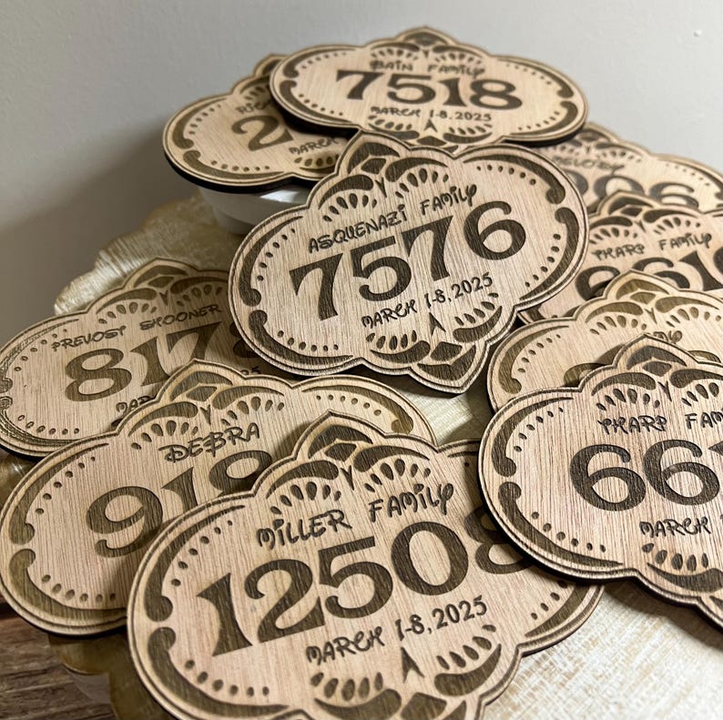 May include: A close-up of a pile of wooden signs with engraved numbers and text. The signs are shaped like a cloud with a decorative border. The text on the signs includes family names and dates.