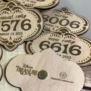 May include: Wooden Disney Treasure magnets with a cloud shape and a magnet on the back. The front of the magnets have a family name, a number, and the year 2025. The back of the magnets have the Disney Treasure logo and the company name "Reds Hot Creations.com".
