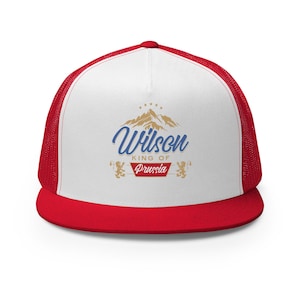 May include: A red and white trucker hat with a red brim and mesh back. The front panel displays the name "Wilson" in blue script above a mountain graphic and the text "KING OF Prussia".