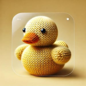May include: A yellow knitted duck toy with black eyes and an orange beak. The duck is sitting on a clear surface.
