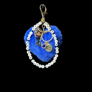 May include: Blue heart-shaped keychain with a small doll charm, a gold ring, and a charm that says "I love my cat". The keychain is attached to a beaded bracelet with the words "TO KILL A MOCKINGBIRD, ENOUGH IS ENOUGH, SHARP EYES" spelled out.