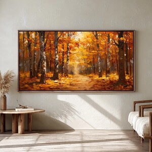 Könnte beinhalten: Ein großer, gerahmter Gemälde zeigt eine lebendige Herbstwaldszene. Das Kunstwerk zeigt hohe Bäume mit orangefarbenem und gelbem Laub, einen Weg und ein warmes, einladendes Licht. Das Gemälde wird an einer neutralen Wand ausgestellt, ergänzt durch einen Holztisch, eine Vase und Stühle.