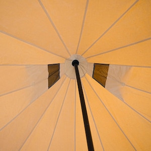 May include: A beige canvas tent with a black center pole. The tent has a circular opening at the top and is supported by multiple radial seams.