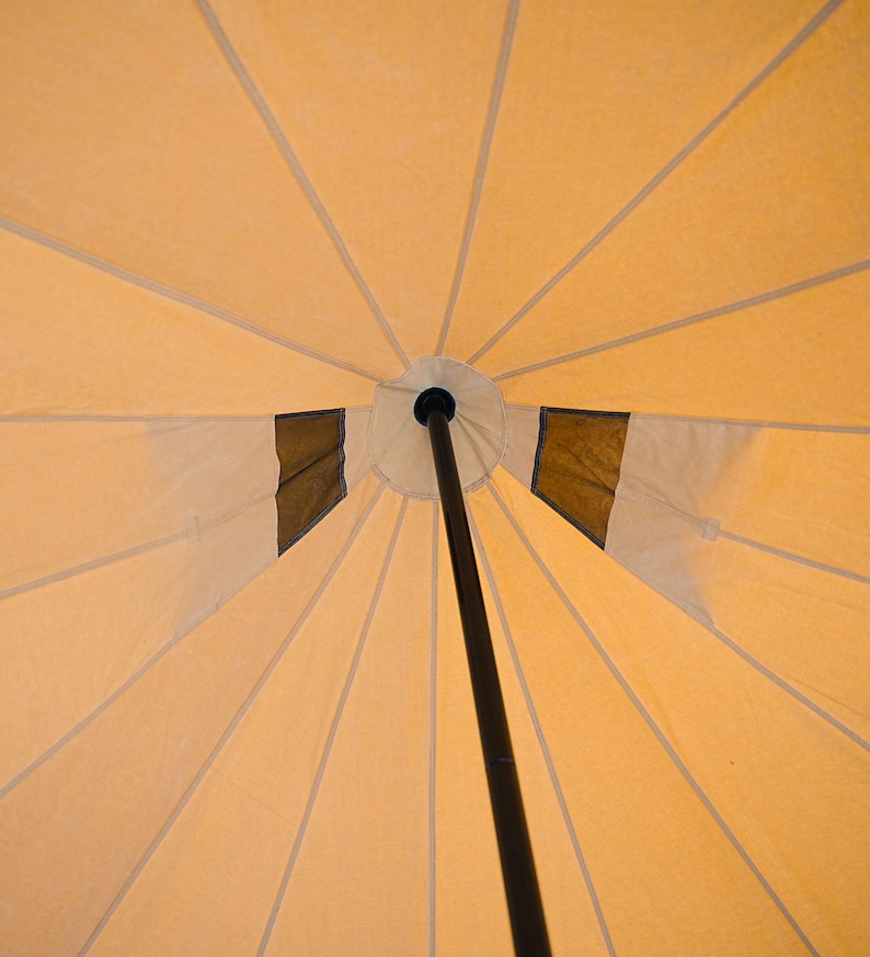 May include: A beige canvas tent with a black center pole. The tent has a circular opening at the top and is supported by multiple radial seams.