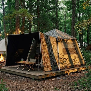 May include: A campsite scene featuring a large tent with a camouflage pattern, set on a wooden platform. A small table and chairs are set up outside. A campfire burns nearby, with other tents visible in the background.