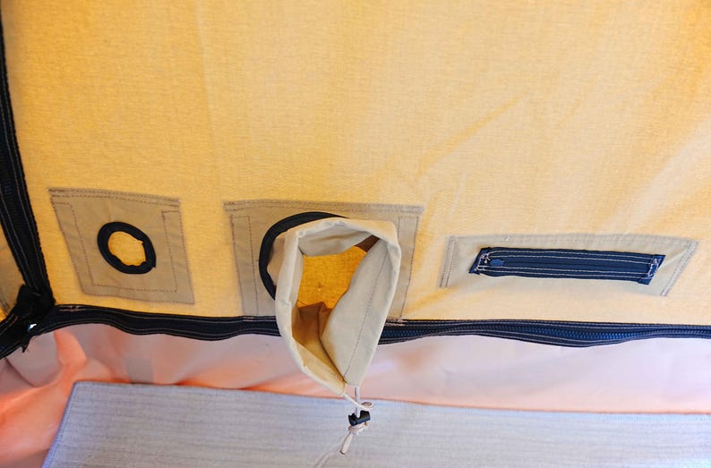 May include: A beige canvas tent with a black zipper and a black fabric flap with a hole in the center. There is a small black zippered pocket on the right side of the image.