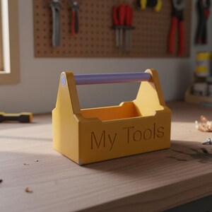 May include: A yellow wooden toolbox with a purple handle and the words "My Tools" engraved on the side. The toolbox is sitting on a wooden surface. Tools are visible in the background.