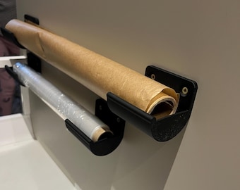 May include: Two black metal wall mounted holders for storing rolls of parchment paper and plastic wrap. The parchment paper is brown and the plastic wrap is clear.