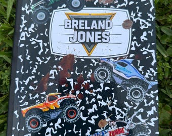 Może przedstawiać: Notatnik kompozycyjny z czarno-białym wzorem i grafiką monster trucków. Notatnik zawiera imię i nazwisko "BRELAND JONES" w białym i złotym emblemacie. Przedstawiono kilka monster trucków w różnych kolorach, wraz z brązowymi plamami błota.