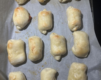 May include: A baking tray lined with baking parchment holds 15 golden brown crescent rolls. The rolls are arranged in three rows of five.