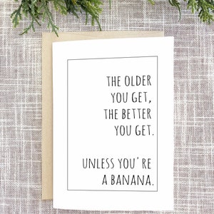 Op de afbeelding: Een witte wenskaart met een zwarte rand en de tekst: "THE OLDER YOU GET, THE BETTER YOU GET. UNLESS YOU'RE A BANANA." De kaart zit in een bruine envelop, met groen op de achtergrond.