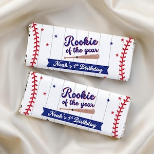 May include: Two rectangular candy bar wrappers featuring a white background with thin vertical black pinstripes, red baseball stitching patterns, blue stars, a brown baseball bat, and the text Rookie of the year Noah's 1st Birthday.