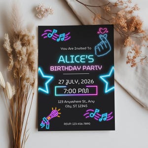 May include: A black rectangular birthday party invitation card featuring neon-style graphics in blue and pink. The text reads: You Are Invited To ALICE'S BIRTHDAY PARTY, 27 JULY, 2026, 7:00 PM, 123 Anywhere St., Any City, ST 12345, and RSVP: 123-456-7890.
