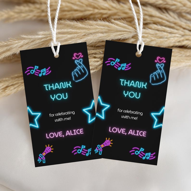 May include: Two rectangular black gift tags with white string loops. The tags feature neon-style graphics including music notes, stars, a microphone, a heart, and a finger heart. Text reads: THANK YOU for celebrating with me! LOVE, ALICE.