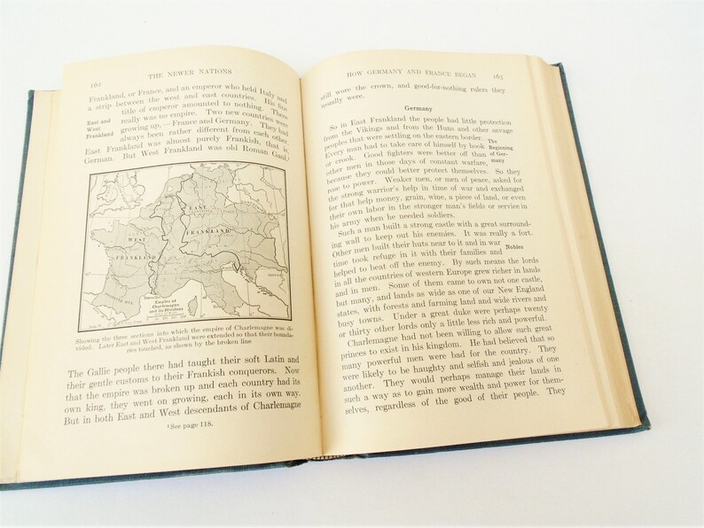 May include: A page from a history book showing a map of Europe with the borders of East and West Frankland highlighted in red. The text on the page discusses the history of the Frankish Empire and the rise of Germany and France.