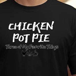 May include: Black t-shirt with the text "CHICKEN POT PIE Three of My Favorite Things" in white. The shirt features a chicken, cannabis leaf, and pie graphic. The shirt is made of a soft material.