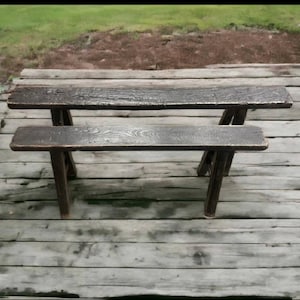 May include: A rustic, dark brown wooden bench set. The set includes a full-size bench and a smaller bench, both with A-frame legs. The wood grain is visible, and the benches appear weathered, suggesting outdoor use. The benches are set on a wooden deck.