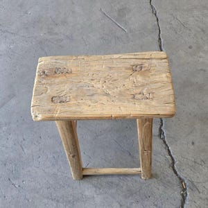 May include: A rustic wooden stool with a rectangular top and four legs. The stool is made of weathered wood and has a natural finish.