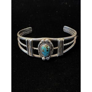 May include: A silver cuff bracelet featuring a central teardrop-shaped turquoise stone with brown matrix. The band consists of two smooth silver wires and two twisted silver wires, accented by two vertical silver bars on each side.