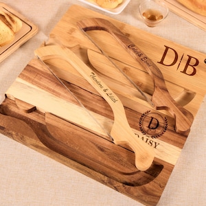 May include: Wooden cheese board set with a square cutting board and three cheese knives. The board has a dark brown and light brown wood grain pattern. The knives are engraved with names and initials. The board also has the word "DAISY" engraved.