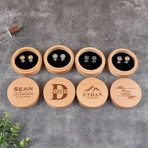 May include: Four round wooden boxes with black velvet inserts, each containing a pair of metal cufflinks. The lids are engraved with names, dates, and designs including SEAN, DAVIS, ETHAN, and Ryan, along with mountain and leaf motifs.