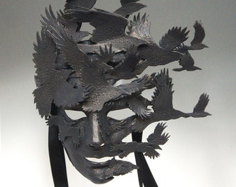 May include: A black leather mask featuring a human face with a design of numerous crows in flight around the face.