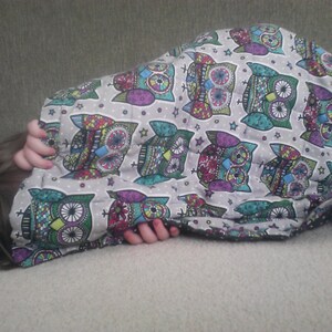 May include: A person is sleeping under a blanket with a colorful owl pattern. The blanket is made of soft fabric and has a white background with multi-colored owls.