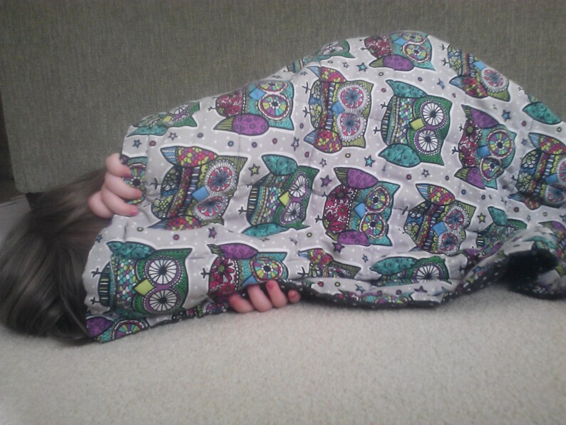 May include: A person is sleeping under a blanket with a colorful owl pattern. The blanket is made of soft fabric and has a white background with multi-colored owls.