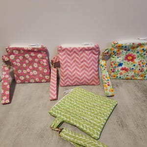 May include: Four small zippered pouches with fabric straps. The pouches are made of pink and green fabric with different patterns. One pouch has a floral pattern, another has a chevron pattern, and the third has a leaf pattern.