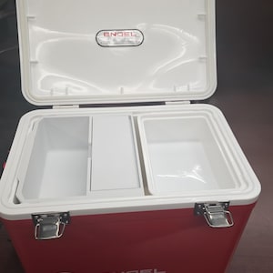 May include: Red and white Engel cooler with the lid open. The cooler has a white interior with two compartments and a divider. The cooler has a capacity of 19 quarts. The Engel logo is visible on the lid and the front of the cooler.