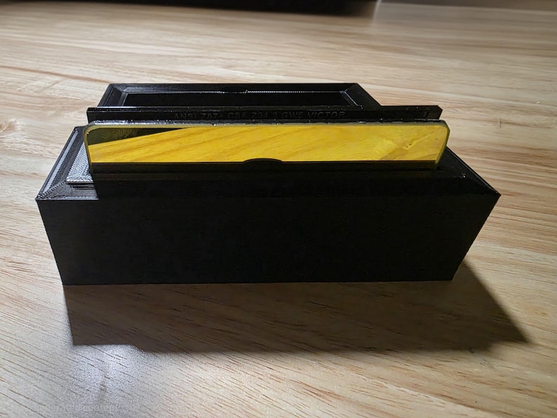 May include: A black rectangular box with a yellow and wood-grain top. The top section has a recessed area. The box is sitting on a wooden surface. The text on the top is blurry.