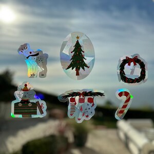 Puede incluir: Un conjunto de siete pegatinas de Navidad iridiscentes con un reno, un árbol de Navidad, una corona, un gato en una media, una media con bastones de caramelo, un bastón de caramelo y una media con estrellas.