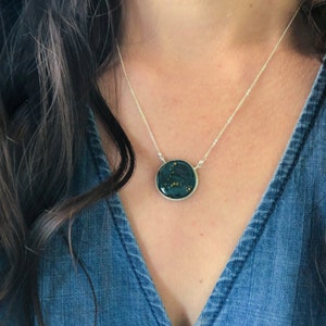 May include: A silver chain necklace with a round pendant featuring a constellation design on a dark green background.