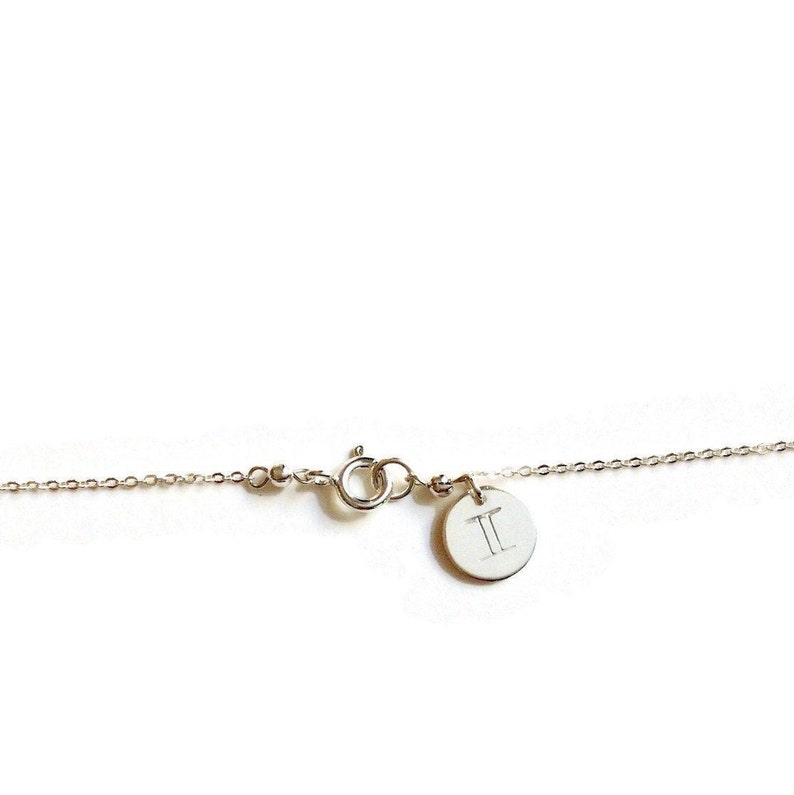 May include: Silver chain necklace with a small round charm featuring the Gemini zodiac symbol.